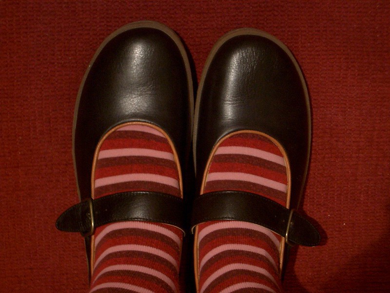 Dos zapatos negros con calcetas de rayas rojas y rosas, como los que la gente dice que deben usar las niñas